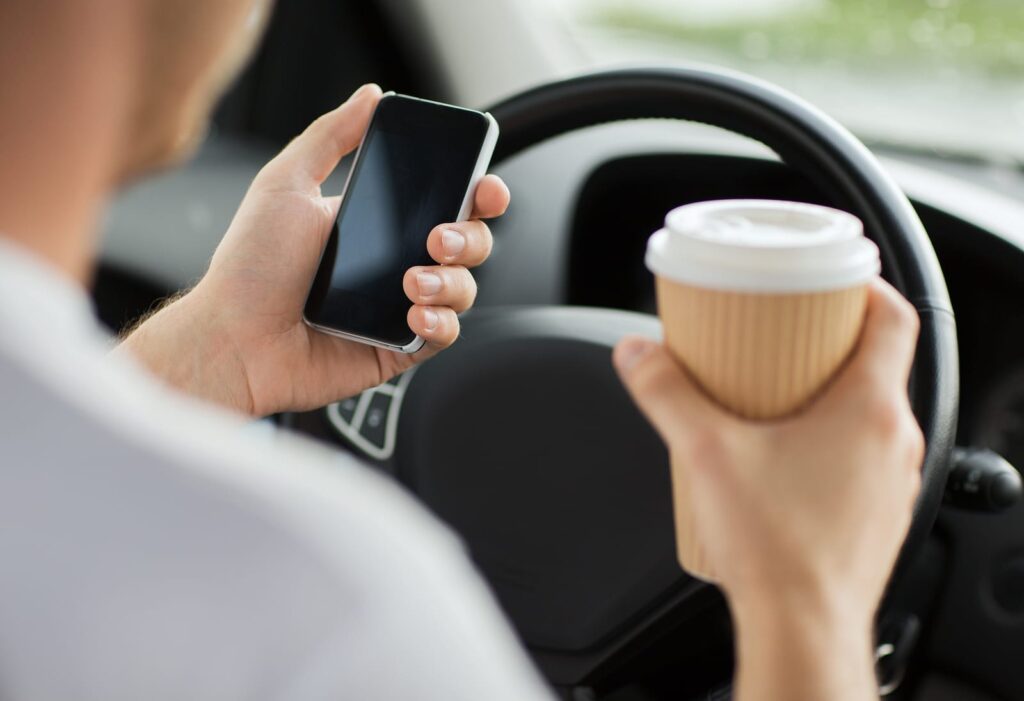 Distracted Driving Accidents involving phone usage transportation and vehicle concept - man drinking coffee and usi