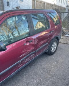 red sport utility vehicle showing major scrape damage to driver's side after accident