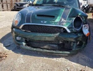 the front end of a green mini cooper's smashed up front end with left headlight knocked out and hanging down