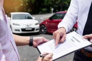 close up shot of a person signing an insurance document on a clipboard another person is holding with car crash scene in the background