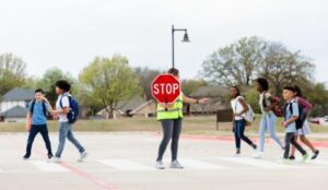 Crossing guard with stop sign directing children across crosswalk on suburban street