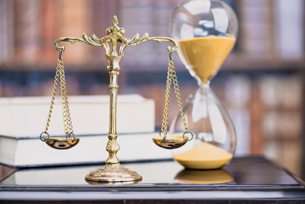 A golden scale of justice balanced next to an hourglass with sand running through, symbolizing the importance of timely action in personal injury legal cases.